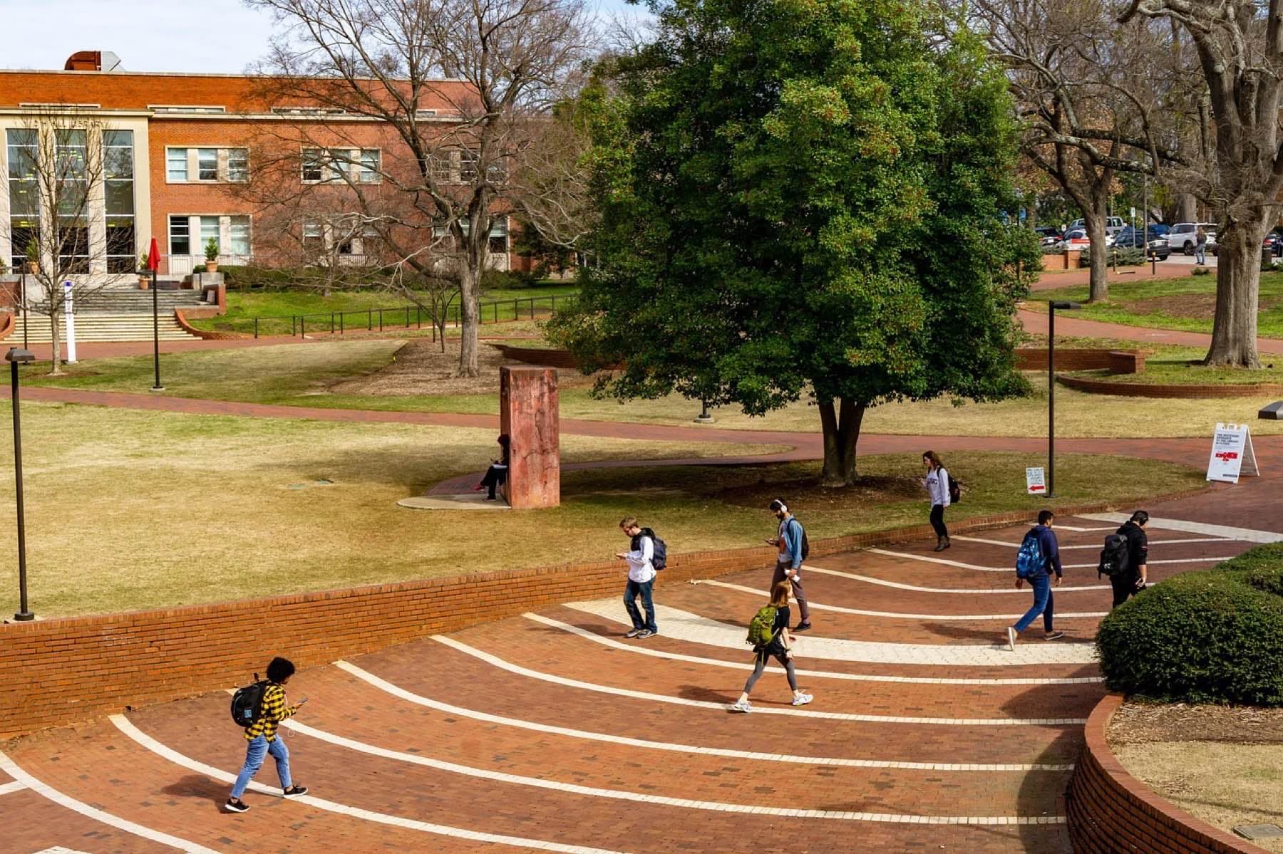 Students walking across a brick-paved college campus on a sunny afternoon